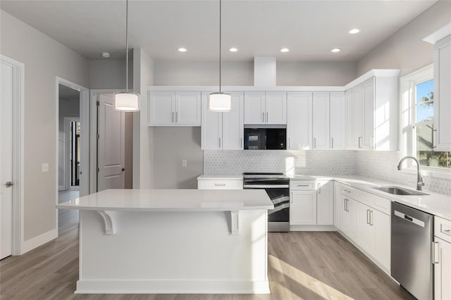 kitchen with white cabinets, appliances with stainless steel finishes, a kitchen island, and pendant lighting