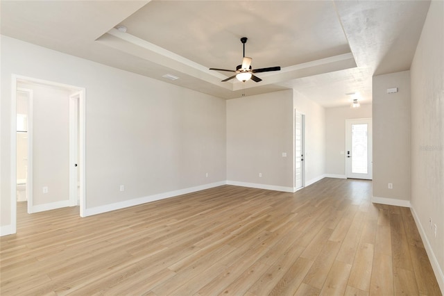 empty room featuring light hardwood / wood-style flooring, ceiling fan, and a tray ceiling