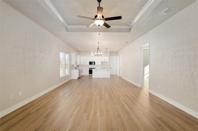 unfurnished living room with ceiling fan with notable chandelier, sink, a tray ceiling, and light hardwood / wood-style floors