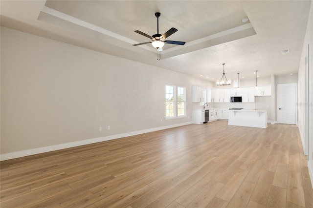 unfurnished living room featuring ceiling fan with notable chandelier, light hardwood / wood-style floors, and a raised ceiling