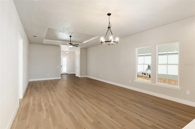 empty room with a raised ceiling, ceiling fan with notable chandelier, and light wood-type flooring