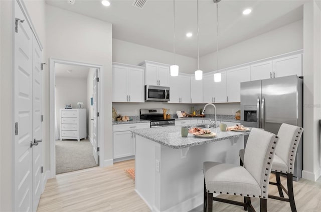 kitchen featuring appliances with stainless steel finishes, a kitchen island with sink, white cabinetry, and decorative light fixtures