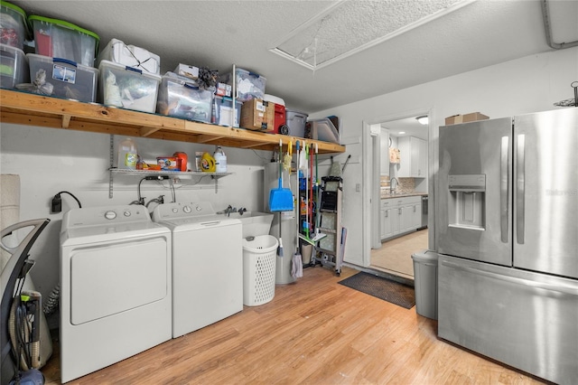 laundry area with light hardwood / wood-style floors, sink, a textured ceiling, and washer and clothes dryer