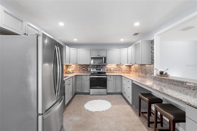 kitchen with stainless steel appliances, decorative backsplash, light stone counters, gray cabinetry, and a breakfast bar area