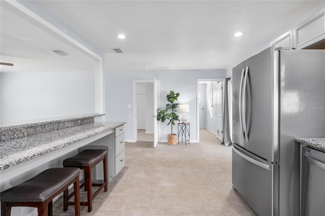 kitchen with light stone countertops, white cabinetry, a breakfast bar, and stainless steel refrigerator