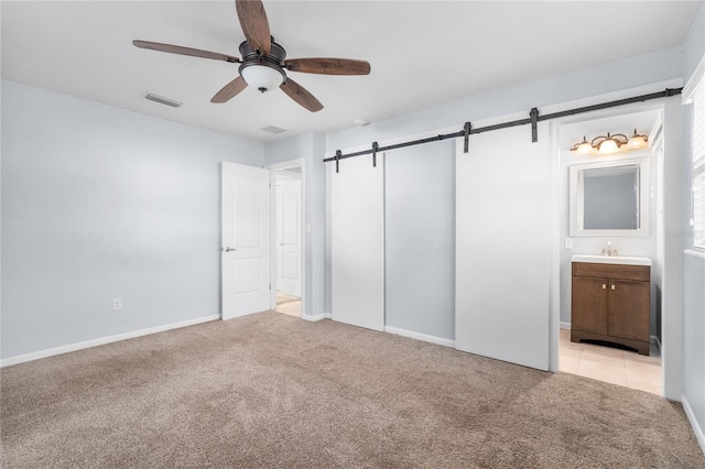 unfurnished bedroom featuring ceiling fan, a barn door, light colored carpet, and connected bathroom