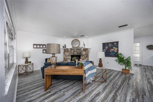 living room with a textured ceiling, crown molding, hardwood / wood-style flooring, and a stone fireplace