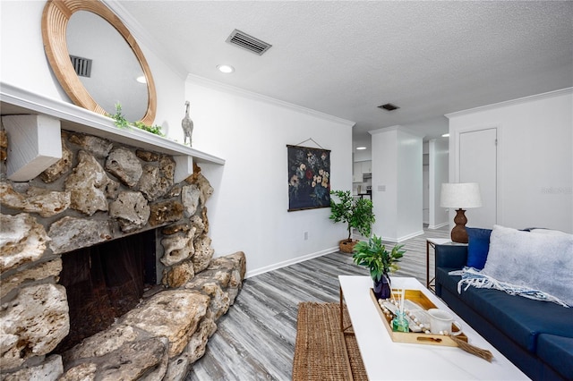 living room featuring crown molding, wood-type flooring, a stone fireplace, and a textured ceiling