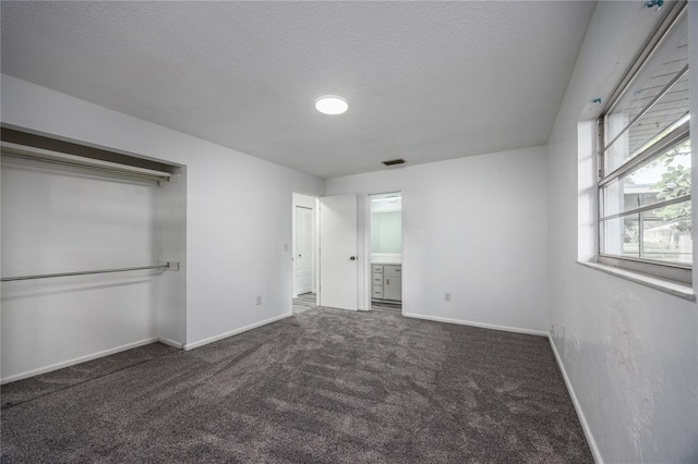 unfurnished bedroom with a textured ceiling, dark colored carpet, and ensuite bath