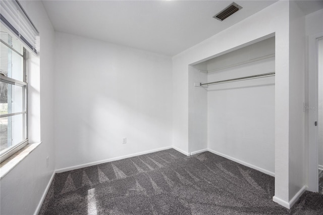 unfurnished bedroom with a closet, multiple windows, and dark colored carpet