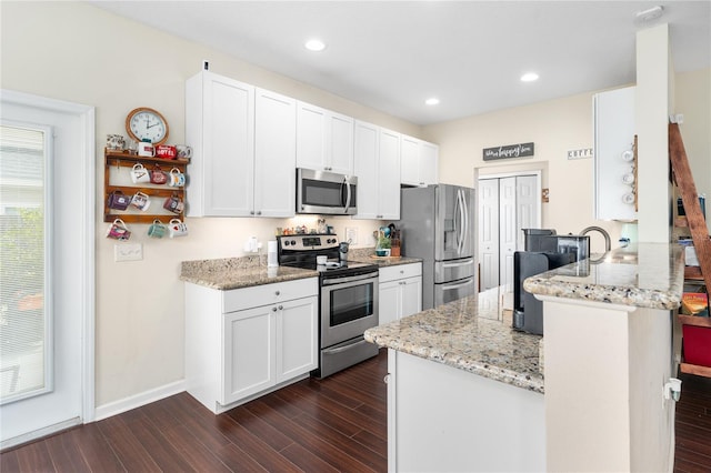 kitchen featuring appliances with stainless steel finishes, white cabinetry, light stone counters, kitchen peninsula, and dark wood-type flooring