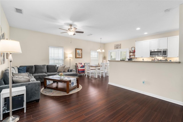 living room with dark hardwood / wood-style flooring, ceiling fan with notable chandelier, and plenty of natural light