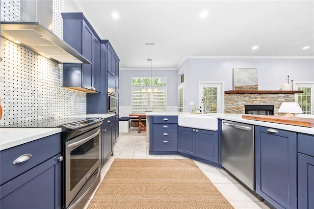 kitchen featuring stainless steel appliances, wall chimney range hood, decorative light fixtures, blue cabinets, and sink