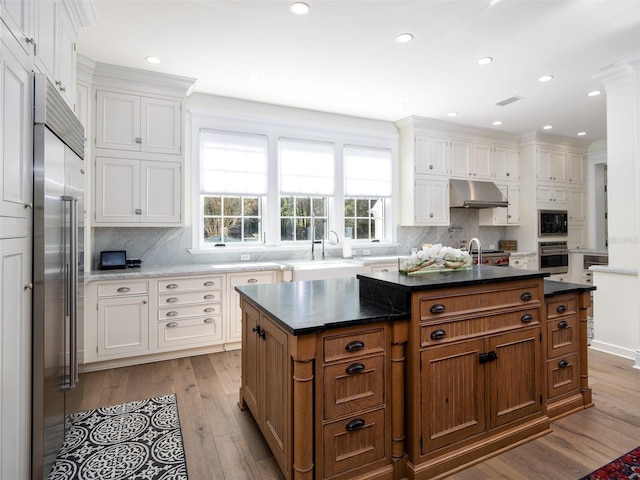 kitchen with white cabinetry, an island with sink, backsplash, built in appliances, and light hardwood / wood-style floors