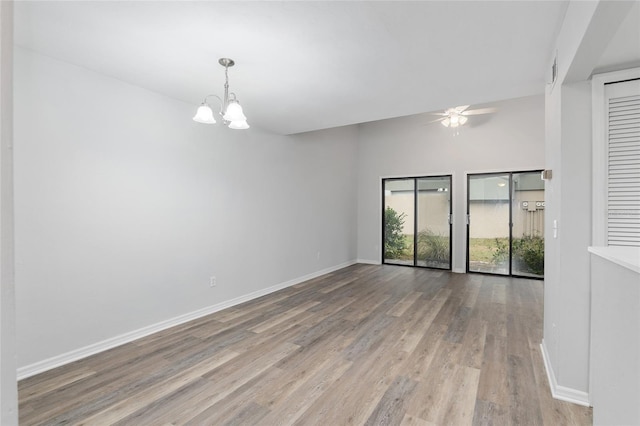 spare room with ceiling fan with notable chandelier, baseboards, and wood finished floors