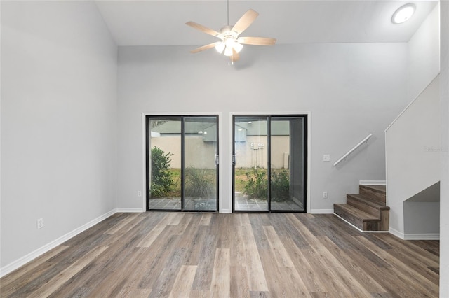 empty room featuring baseboards, stairway, ceiling fan, and wood finished floors