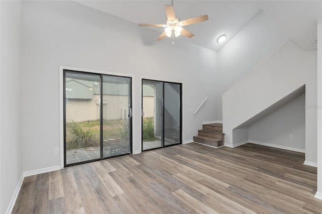 unfurnished living room featuring a ceiling fan, stairs, baseboards, and wood finished floors