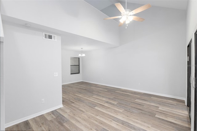 empty room featuring baseboards, visible vents, wood finished floors, high vaulted ceiling, and ceiling fan with notable chandelier