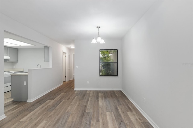 unfurnished dining area with a notable chandelier, wood finished floors, and baseboards