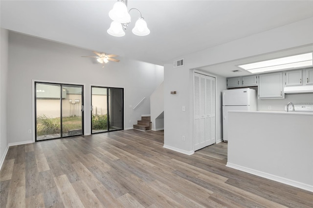 unfurnished living room featuring stairs, visible vents, light wood-style floors, baseboards, and ceiling fan with notable chandelier