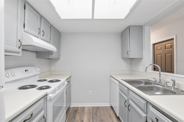 kitchen featuring under cabinet range hood, white appliances, wood finished floors, a sink, and light countertops