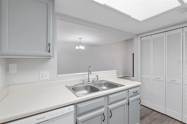 kitchen featuring a peninsula, wood finished floors, a sink, light countertops, and dishwasher