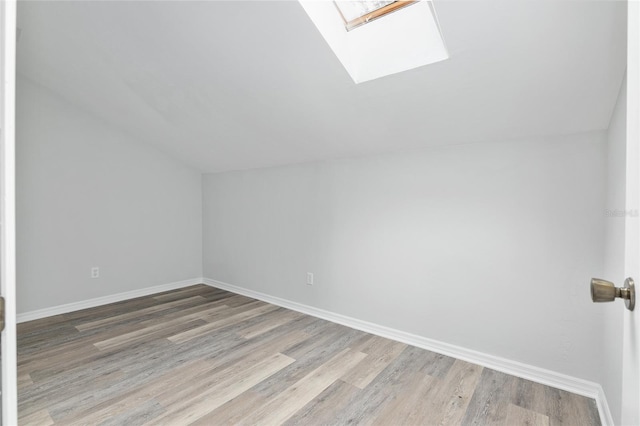 additional living space featuring light wood-style floors, vaulted ceiling with skylight, and baseboards