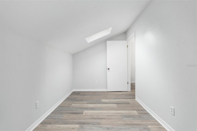 additional living space with vaulted ceiling with skylight, baseboards, and wood finished floors