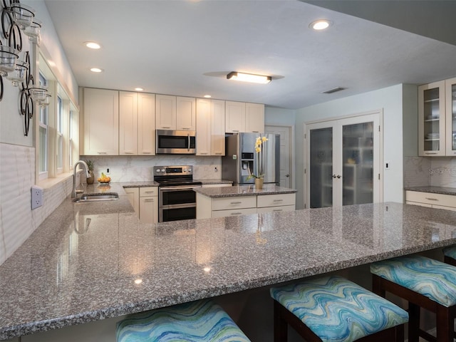 kitchen with white cabinetry, sink, dark stone countertops, a breakfast bar area, and stainless steel appliances