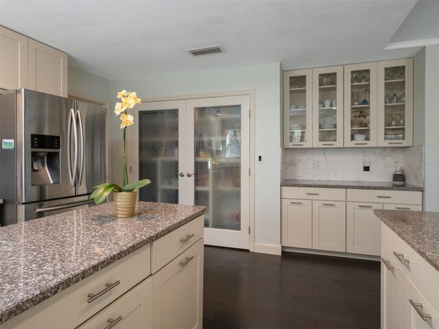 kitchen featuring dark wood-type flooring, backsplash, stainless steel fridge, and light stone counters