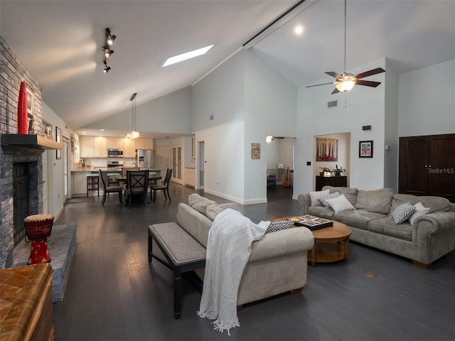 living room with ceiling fan, a skylight, high vaulted ceiling, dark hardwood / wood-style flooring, and a brick fireplace