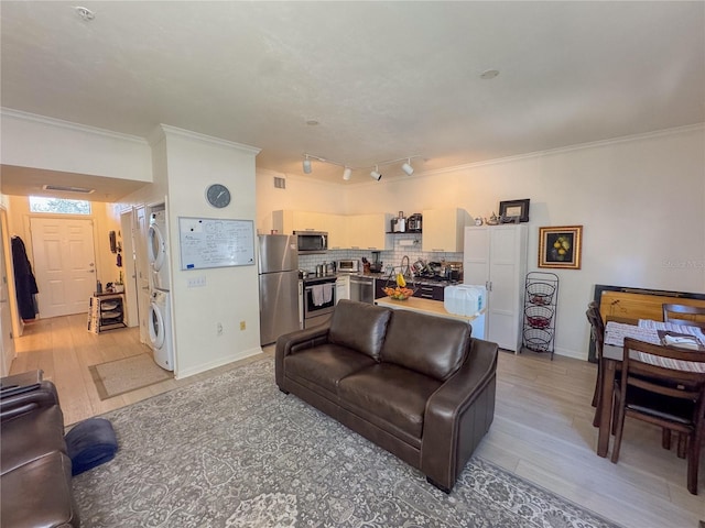 living room with ornamental molding, stacked washer and clothes dryer, light hardwood / wood-style flooring, and rail lighting