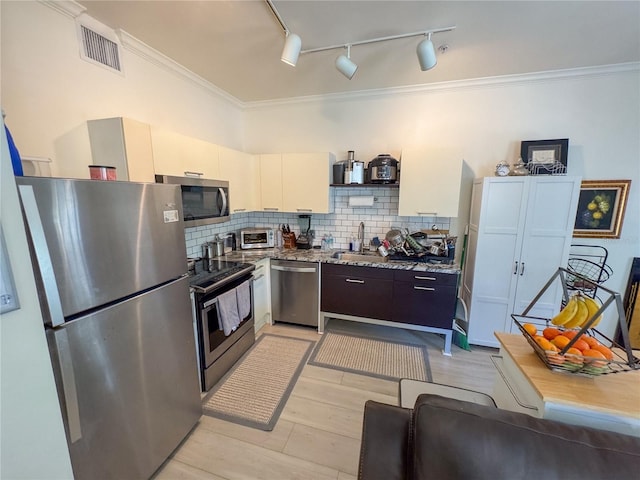 kitchen featuring white cabinetry, track lighting, ornamental molding, appliances with stainless steel finishes, and decorative backsplash