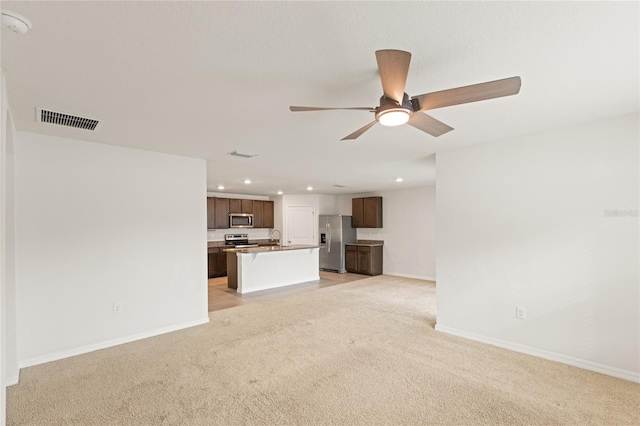 unfurnished living room featuring light carpet, ceiling fan, and sink