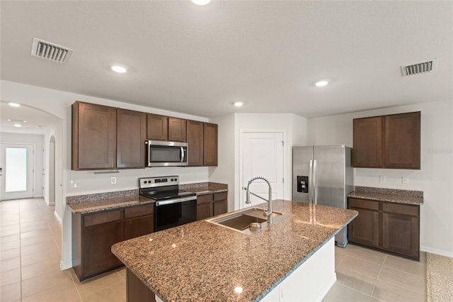 kitchen featuring light tile patterned floors, appliances with stainless steel finishes, a kitchen island with sink, dark brown cabinetry, and sink