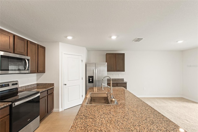 kitchen featuring a textured ceiling, appliances with stainless steel finishes, dark brown cabinetry, sink, and light colored carpet