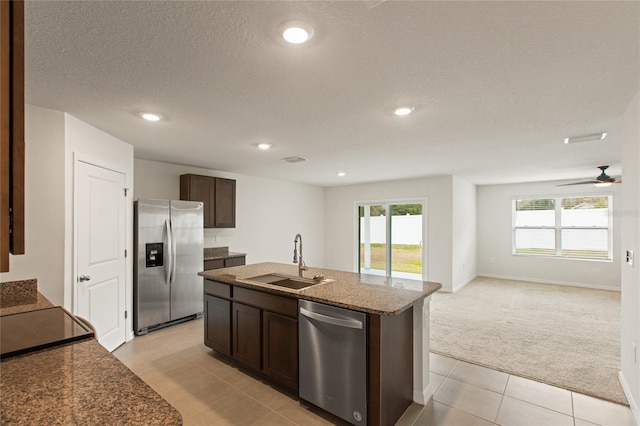 kitchen with dark brown cabinetry, appliances with stainless steel finishes, sink, a kitchen island with sink, and light colored carpet