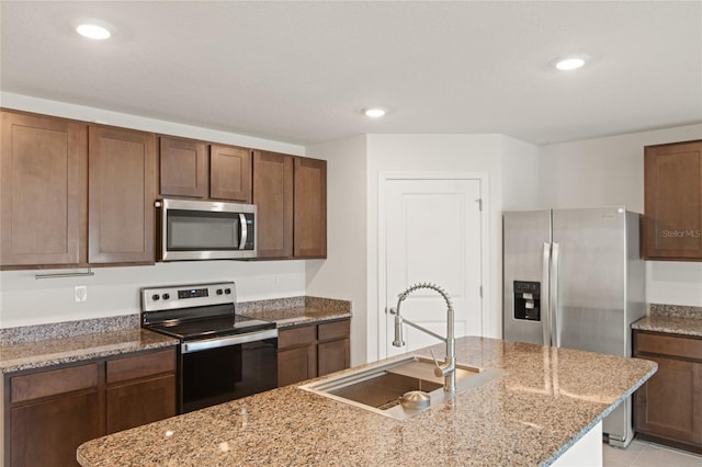 kitchen with a center island with sink, sink, stainless steel appliances, light tile patterned floors, and light stone counters