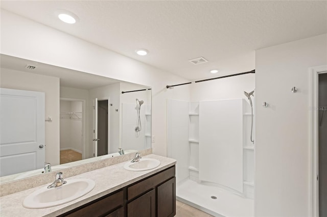 bathroom with a textured ceiling, a shower, tile patterned flooring, and vanity