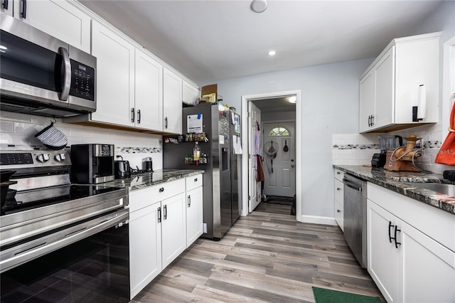 kitchen featuring decorative backsplash, white cabinetry, stainless steel appliances, and dark stone countertops