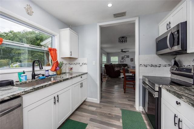 kitchen featuring appliances with stainless steel finishes, white cabinetry, dark stone countertops, sink, and ceiling fan