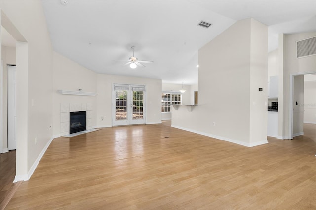 unfurnished living room with french doors, vaulted ceiling, light hardwood / wood-style flooring, ceiling fan, and a tiled fireplace