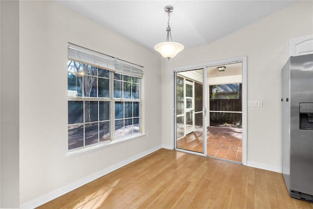 unfurnished dining area featuring vaulted ceiling and light hardwood / wood-style flooring