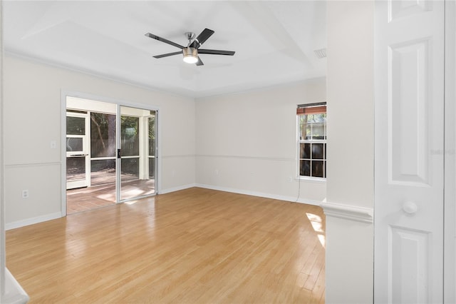 empty room with ceiling fan, light wood-type flooring, and a tray ceiling