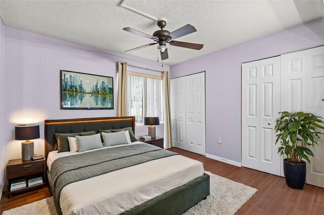 bedroom featuring ceiling fan, multiple closets, dark hardwood / wood-style floors, and a textured ceiling