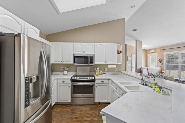 kitchen with white cabinets, appliances with stainless steel finishes, sink, kitchen peninsula, and vaulted ceiling