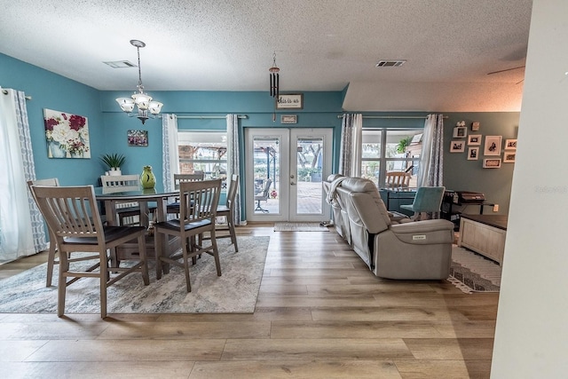 dining area featuring a textured ceiling, a chandelier, wood-type flooring, and french doors