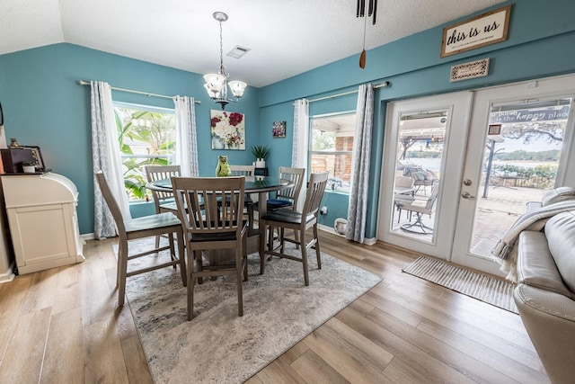 dining space with vaulted ceiling, a notable chandelier, light wood-type flooring, a textured ceiling, and french doors