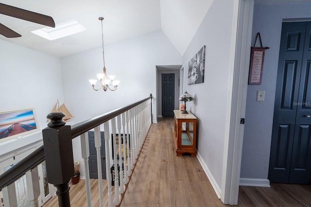 hallway with lofted ceiling with skylight, an inviting chandelier, and hardwood / wood-style floors