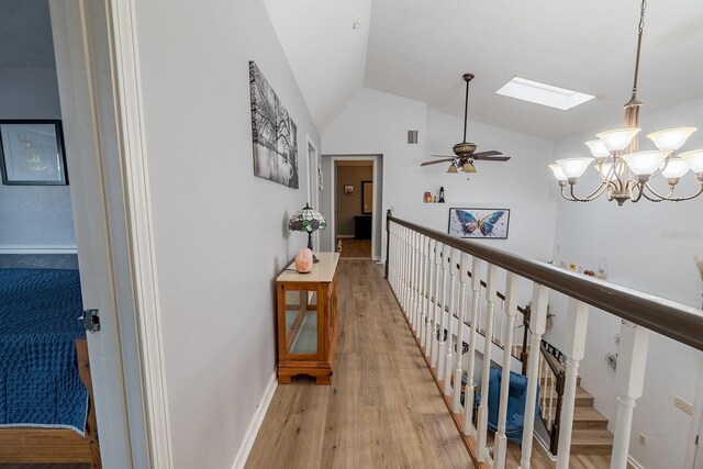 corridor featuring light hardwood / wood-style floors, lofted ceiling with skylight, and a chandelier